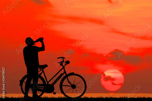 Silhouette man and bike relaxing on blurry sky background.