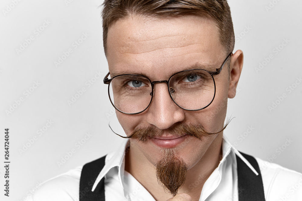 Close up picture of attractive positive banker with handlebar mustache, goatee beard and smart blue eyes looking at camera with confident facial expression, smiling. People, lifestyle and business Close up picture of attractive positive banker with handlebar mustache, goatee beard and smart blue eyes looking at camera with confident facial expression, smiling. People, lifestyle and business