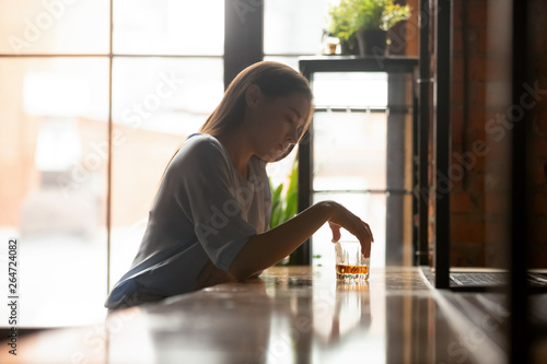 Young sad woman sitting on bar counter drinking alcohol drinks