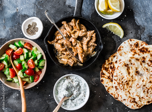 Foto Ingredients for greek chicken gyros - fried chicken, tomato cucumber salad, tzatziki sauce and flatbread on a dark background, top view