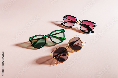 Set of Stylish sunglasses with bright sunlight on pale pink background. Flat lay, top view. Summer fashion concept