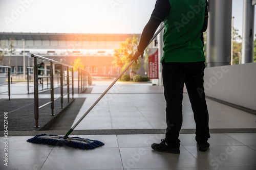 cleaner with mop and uniform cleaning hall floor of public business building