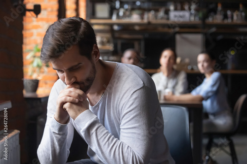 Sad guy sitting alone separately from other mates in cafe
