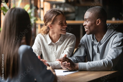 Diverse happy couple sitting at table with real estate agent