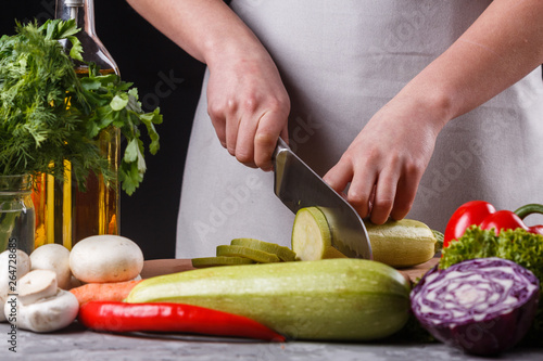 young woman in a gray apron cuts a zucchini