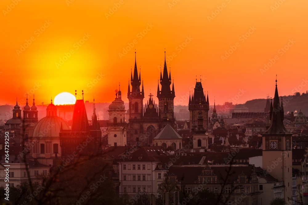 View of orange and pink sky during morning sunrise in Prague, capital of the Czech Republic, sun shining behind black horizon with towers and spires, urban landscape