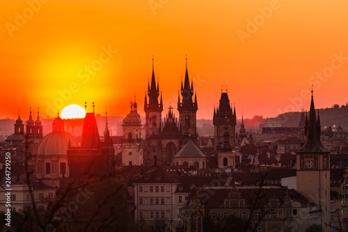 View of orange and pink sky during morning sunrise in Prague, capital of the Czech Republic, sun shining behind black horizon with towers and spires, urban landscape