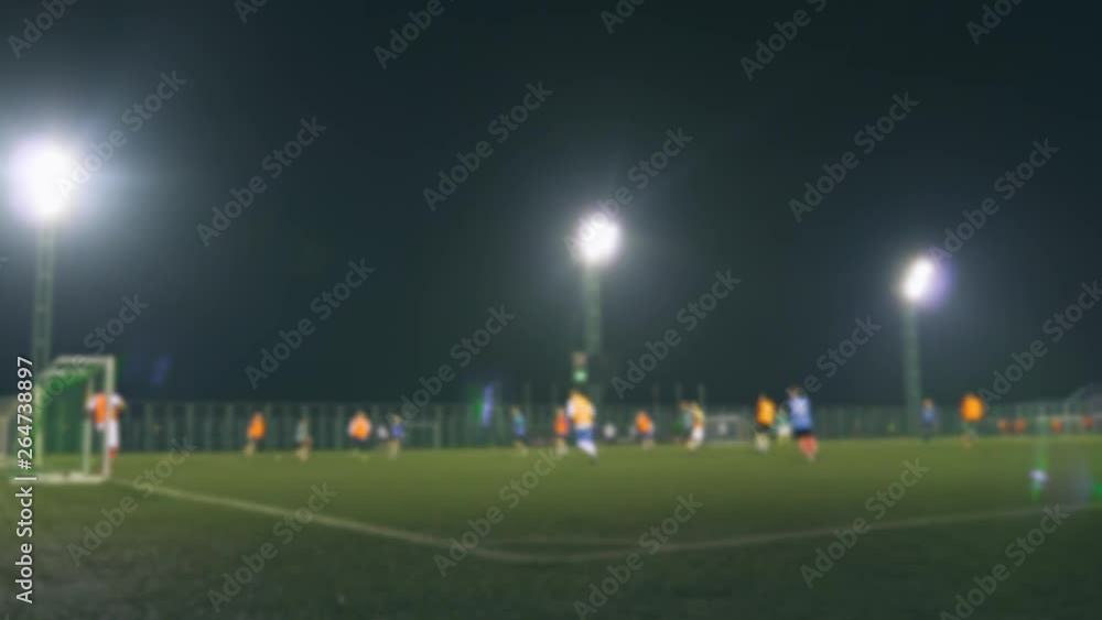 Evening football game. Football players play on the training field, illuminated by stadium lights. Blurred video. Evening football game. Football players play on the training field, illuminated by stadium lights. Blurred video.