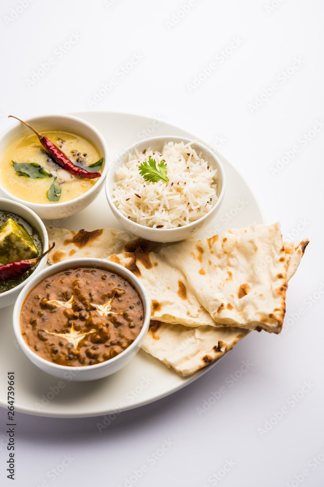 Indian vegetarian  platter / Thali having Palak paneer butter masala, dal makhani, flat bread or naan and rice served in a white plate