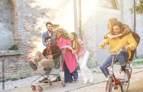 Crazy friends making a racing challenge with shopping cart and bike - Multiracial group of young people having fun outside photo