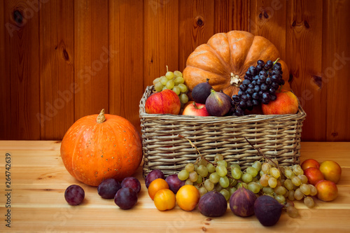 Wicker basket with pumpkins and fresh fruits on wooden table.