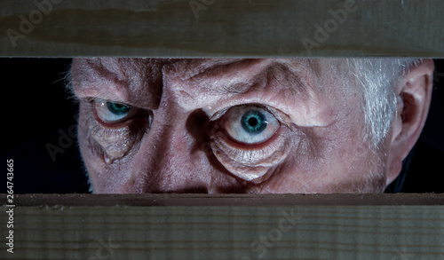 Portrait of a man looking evil from a hiding place. Concept evil, old man.