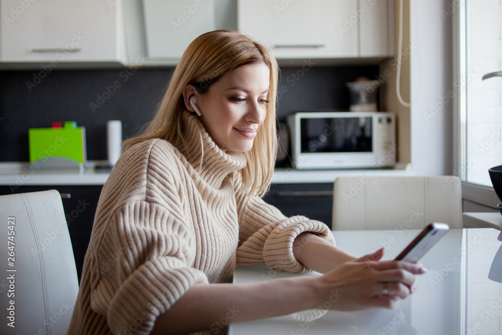 beautiful young woman in a cozy sweater sits in the kitchen and watches updates on social networks. beautiful young woman in a cozy sweater sits in the kitchen and watches updates on social networks.
