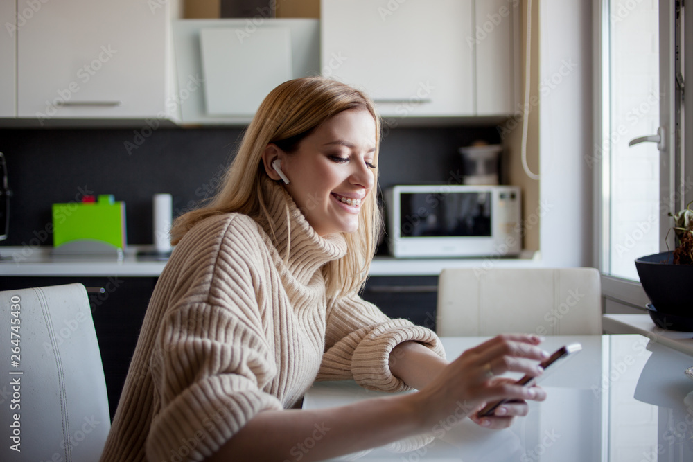 beautiful young woman in a cozy sweater sits in the kitchen and watches updates on social networks. beautiful young woman in a cozy sweater sits in the kitchen and watches updates on social networks.