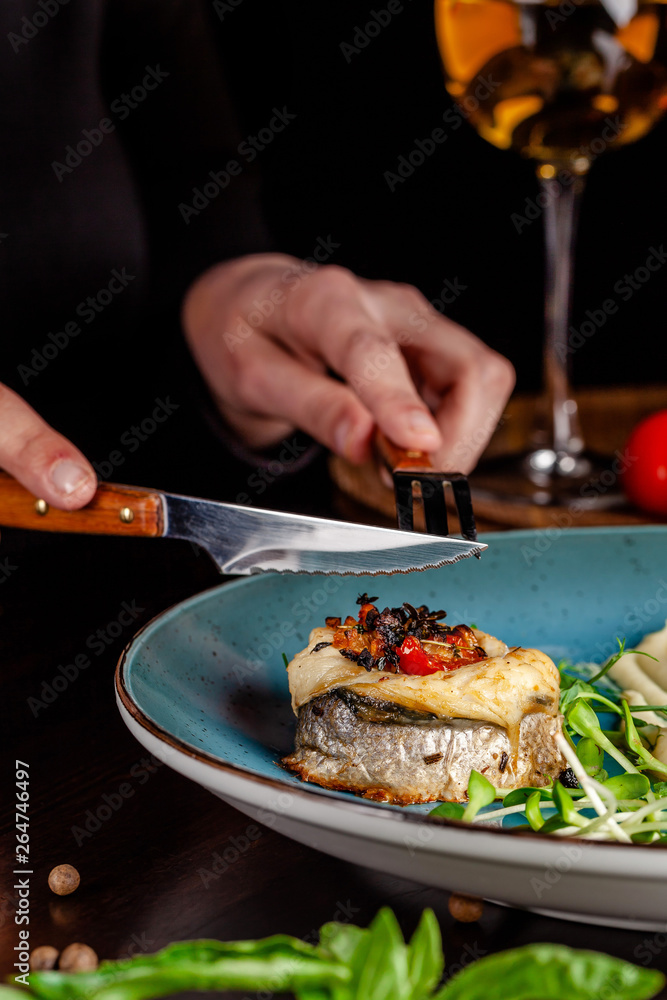 The concept of Italian cuisine. A girl in a restaurant holds a fork and a knife in her hands, and there is a sea bass fish with cardato mash. near a glass of red wine. copy space