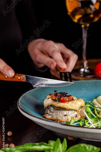 The concept of Italian cuisine. A girl in a restaurant holds a fork and a knife in her hands, and there is a sea bass fish with cardato mash. near a glass of red wine. copy space