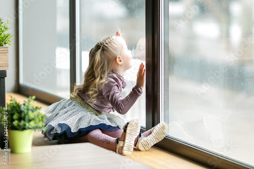 Fotografie A beautiful child is sitting near a large window