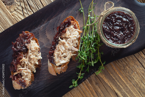pulled pork sandwiches with red onion jam on black serving board decorated with fresh thyme and a glass jar with the pork covered by the jam