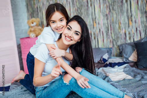 The image of two happy  little and older  sisters sitting on the bed in the room and smiling! © Тарас Нагирняк