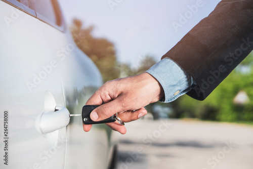 Closeup of a man's hand inserting a key into the door lock of a car. Horizontal format. Car and man are unrecognizable