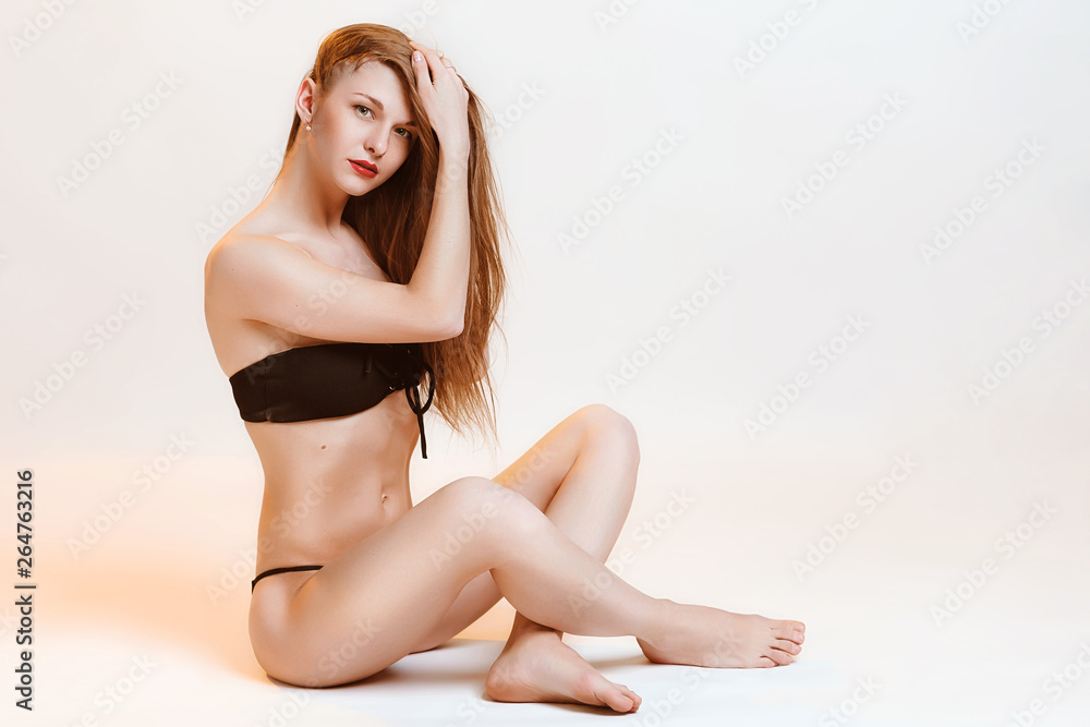 Obraz premium Beautiful sporty girl in black bikini posing in studio. Photo of attractive blonde girl with slim sport toned body. Beauty and body care concept, warm tone color