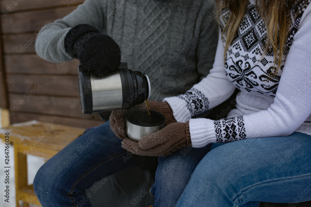 Fototapeta premium A pair of young children drinking tea from a thermos in the winter in the house, a Metal Cup from a thermos on the nature