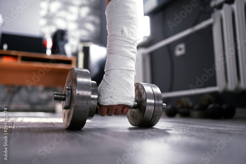 Wide angle photo of broken fractured hand in plaster cast holding dumbbell. Home trainig rehabilitaion after accident. photo