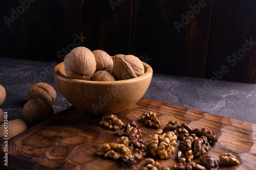 Walnuts in wooden bowl on wooden carved board, side view. Healthy nuts and seeds composition. photo