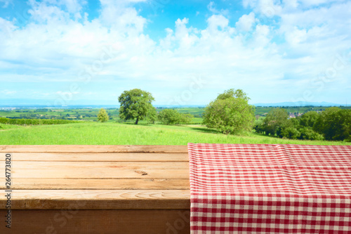 Empty wooden table with tablecloth over summer meadow background