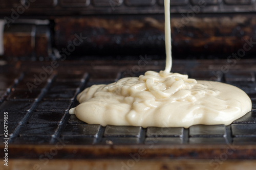 White batter into the waffle iron baking waffles Waffle batter on the hot surface of waffle maker for baking delicious crispy wafers for dessert or Breakfast 