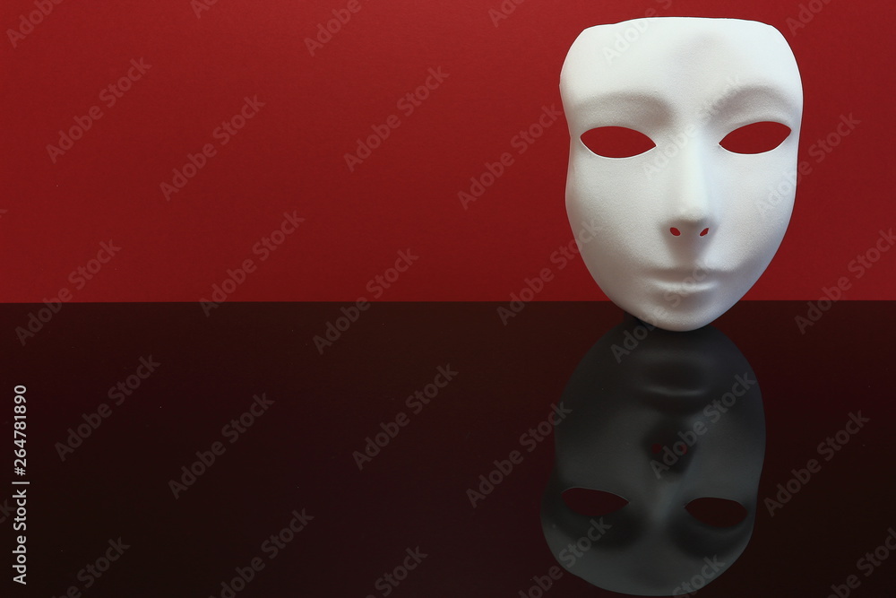 A color image of a white masquerade mask with a red background, reflecting on a black foreground.