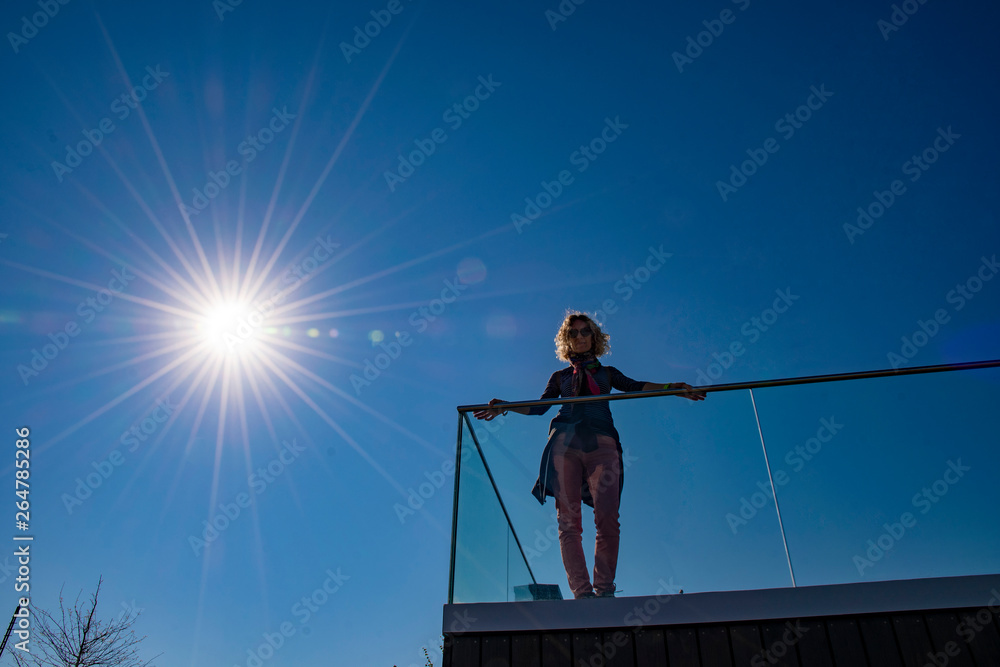 young woman standing on the top of a house with blue sky and sun young woman standing on the top of a house with blue sky and sun
