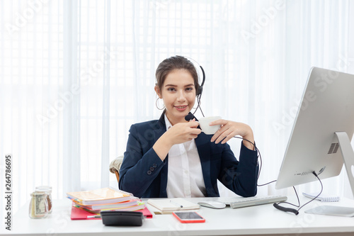 Call center worker. Smiling operator woman holding coffee with headset and computer at office.