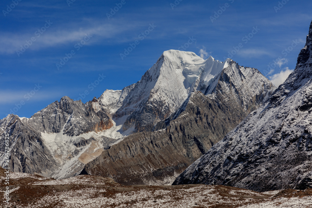 Chenadorje, holy snow mountain in Daocheng Yading Nature Reserve - Garze, Kham Tibetan Pilgrimage region of Sichuan Province China. Clouds blowing off the top of snow capped mountain
