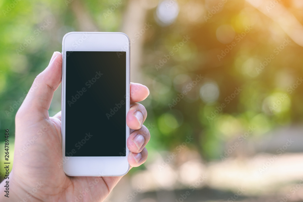 Hand holding smartphone on bokeh nature background