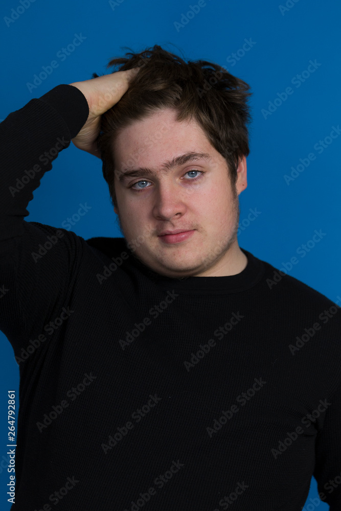 Fototapeta premium Vertical photo of round faced blue eyed teenager boy in dark sweater combing his thick brown hair with his right hand