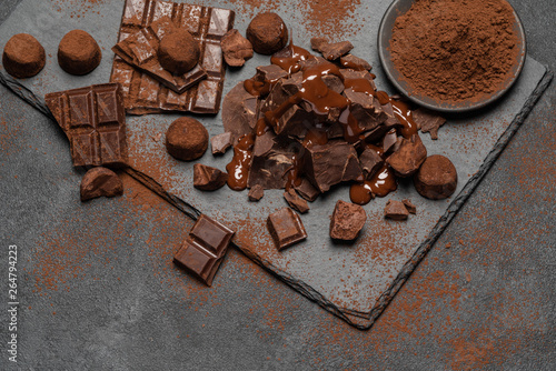 dark or milk chocolate pieces, chocolate syrup and truffle candies on dark concrete background