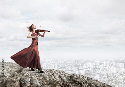 Fotografia Woman violinist in red dress playing melody against cloudy sky