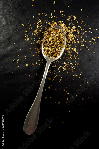 Top view of a spoon with oregano powder isolated on black