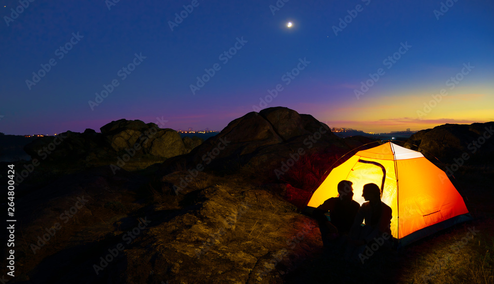 Young Couple Sitting near Illuminated Tent and Looking at Each Other at Beautirul Evening in the Mountains