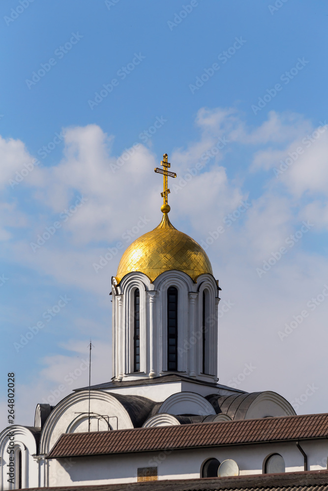 Obraz premium Golden dome of the Orthodox Church with a cross against the blue sky with clouds.