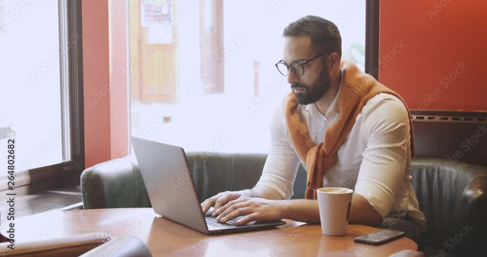Adult bearded man dressed in white shirt working on laptop in modern cafe Adult bearded man dressed in white shirt working on laptop in modern cafe
