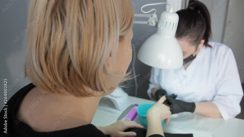 professional manicurist in a medical black mask and black gloves makes a manicure for a woman professional manicurist in a medical black mask and black gloves makes a manicure for a woman