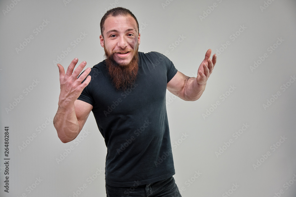 Young brutal man with a beard, bodybuilder in a black t-shirt is standing, posing, talking on a white background with emotions. Beautiful male body. Concept art. Young brutal man with a beard, bodybuilder in a black t-shirt is standing, posing, talking on a white background with emotions. Beautiful male body. Concept art.