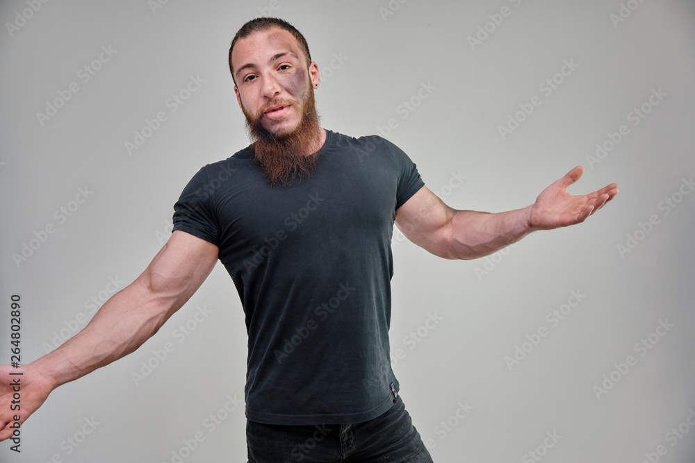 Young brutal man with a beard, bodybuilder in a black t-shirt is standing, posing, talking on a white background with emotions. Beautiful male body. Concept art. Young brutal man with a beard, bodybuilder in a black t-shirt is standing, posing, talking on a white background with emotions. Beautiful male body. Concept art.