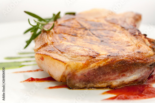 juicy piece of fried pork chop with rosemary and tomato sauce on a white plate close-up