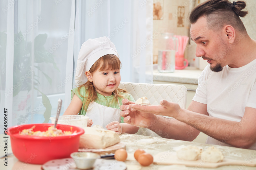 man teaches a child to cook.the process of cooking in a bright kitchen. home cooking is the father of one daughter and love to cook. the child was very surprised by what he saw. dad surprised daughter man teaches a child to cook.the process of cooking in a bright kitchen. home cooking is the father of one daughter and love to cook. the child was very surprised by what he saw. dad surprised daughter