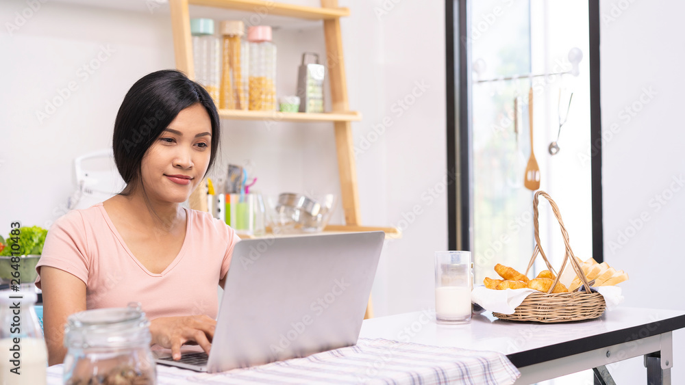 Asian woman or Modern cooks use laptop computers to find information about cooking and nutrition for health and kids. food, life and family concept Asian woman or Modern cooks use laptop computers to find information about cooking and nutrition for health and kids. food, life and family concept