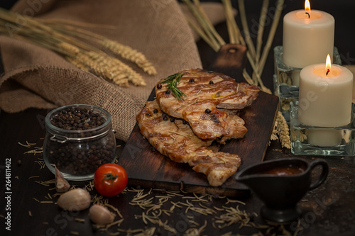 Delicious beef or pock steaks on wooden table. With the ingredients organic for cooking. Tomato and garlic. There are candles on the table. 