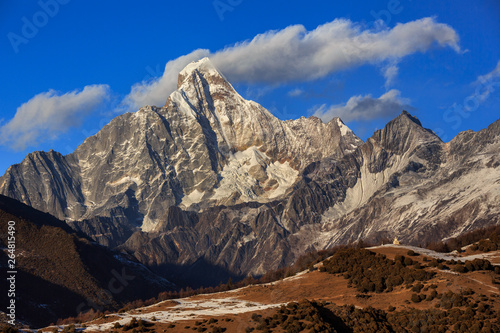 Four Girls Mountain National Park near Xiaojin, Sichuan Province China. Yaomei Peak Summit, blue sky and clouds, White Tibetan Stupa on top of hill in foreground. Mount Siguniang, Hiking Destination photo